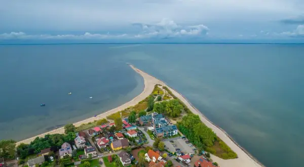 Malownicza miejscowość nad morzem z zabudowaniami i piaszczystą plażą, otoczona spokojnymi wodami.