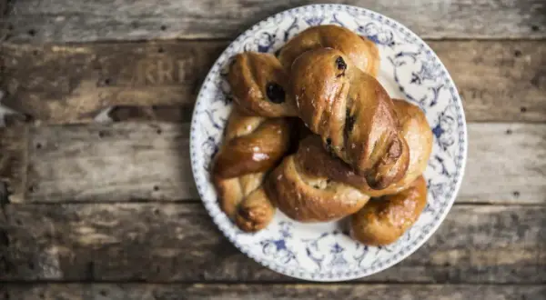 Piatto con biscotti di mosto marchigiani, intrecciati e dorati, su un tavolo di legno rustico.