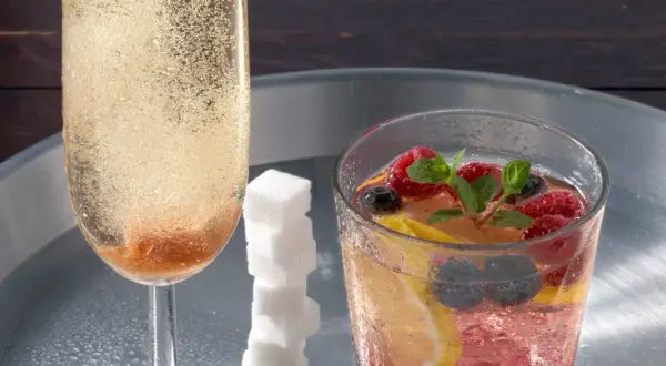 Ein prickelnder Champagner-Cocktail mit Beeren und Zitrone, daneben ein Glas mit sprudelndem Champagner und Zuckerspiralen.