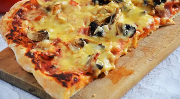 Pyszna pizza capriciosa z pieczarkami i szynką, roztopionym serem, na drewnianej desce.