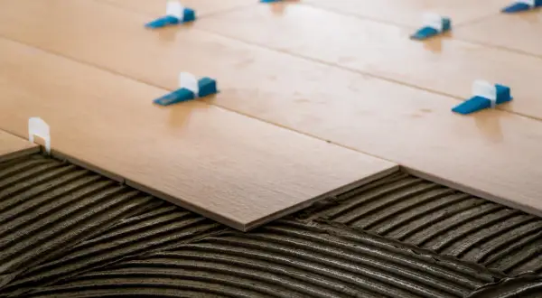 Pose de carrelage en quinconce sur lit de mortier. Des cales bleues et blanches assurent l'espacement régulier des lames imitation bois.