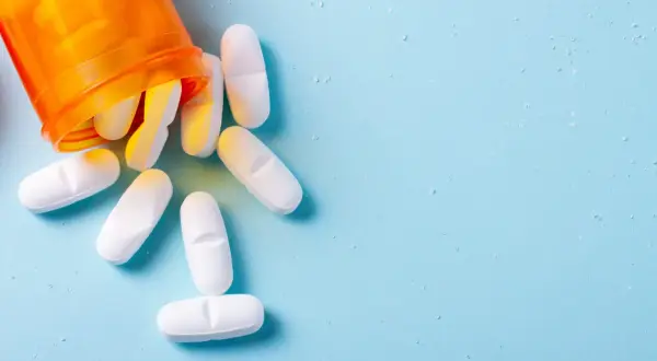 Białe tabletki, w tym euthyrox 25, wysypują się z pomarańczowego pojemnika na jasnoniebieskim tle.
