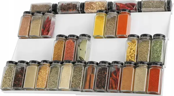 Biały, trójstopniowy organizer na przyprawy wypełniony różnorodnymi ziołami i suszonymi papryczkami chili.