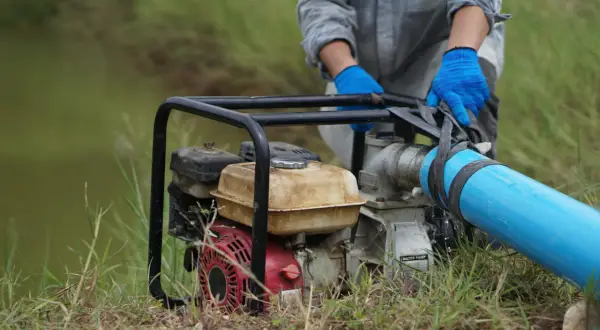 Maintenant, comment démonter une pompe à eau de jardin : une personne en gants bleus manipule le tuyau d'une pompe à eau.