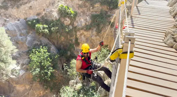 Man i gul hjälm klättrar på en hängbro längs Caminito del Rey, en dramatisk klippstig.