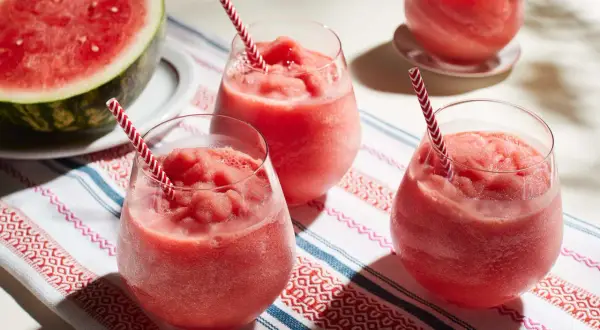 Fryst sallad med vattenmelon i glas med randiga sugrör. En halv vattenmelon ligger bredvid.