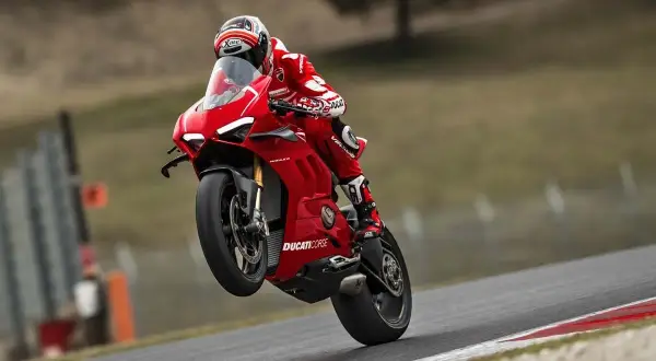 Czerwona Ducati Panigale V4R na torze, z przednim kołem w powietrzu. Kierowca w kombinezonie Ducati Corse.