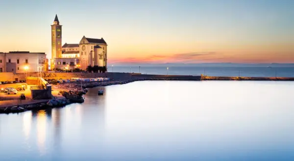 Tramonto sul porto di Trani, con la cattedrale illuminata che domina il paesaggio. Un'incantevole vista dei dintorni di Trani.
