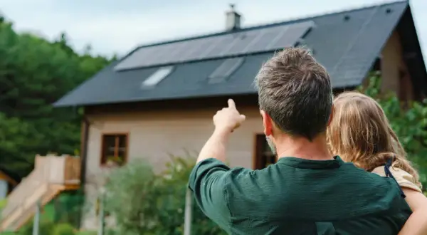 Hombre señala las placas solares virtuales en el tejado de una casa, mientras abraza a una niña.