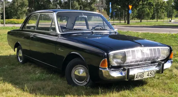 Svart Ford Taunus 1964, en klassisk bil med kromdetaljer, parkerad på en gräsmatta.