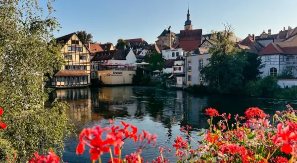 Blick auf Bamberg mit Fachwerkhäusern am Fluss. Rote Geranien im Vordergrund. Entdecken Sie Bamberg Geheimtipps!