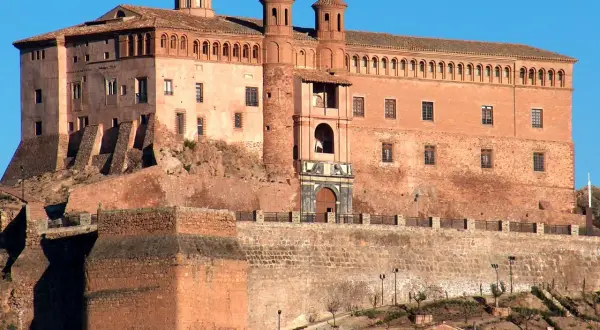 Imponente castillo de ladrillo rojo, con torres y cúpulas, coronando una colina. Un lugar perfecto para imaginar el festival de los castillos.
