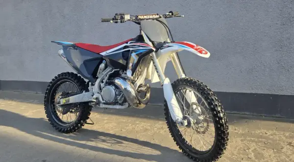 Motocykl crossowy Husqvarna CR 250 z czerwonym siedzeniem i czarnymi elementami, gotowy do jazdy po torze.