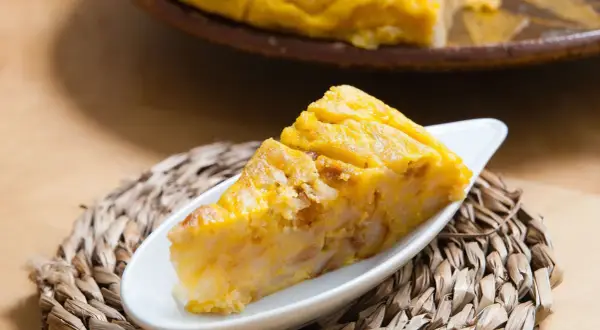 Una porción de tarta de choclo, dorada y apetitosa, servida en un plato blanco sobre una esterilla tejida.