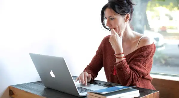 Kobieta przy laptopie, zamyślona, jakby udawała kogoś innego, by zdobyć nowe informacje.