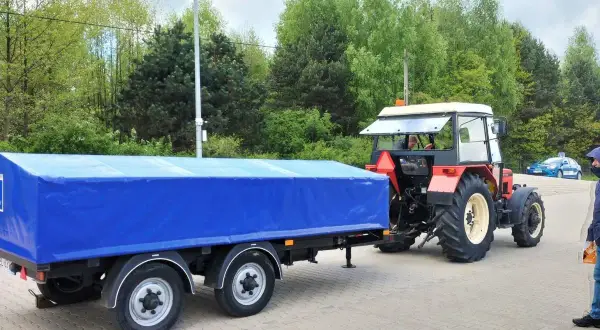 Czerwony traktor z niebieską plandeką na przyczepie. Zastanawiasz się, prawo jazdy kat T od ilu lat?