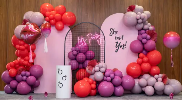 Różowa girlanda balonowa tworzy tło dla imprezy. Napis "She said Yes!" i neonowe "Let's Party" dodają uroku.