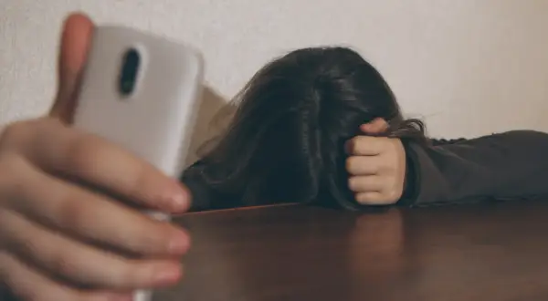 Osoba z telefonem w dłoni, ukrywająca twarz we włosach. Czy to próba ukrycia smutku, czy tylko pozowanie? Człowiek dwulicowy.