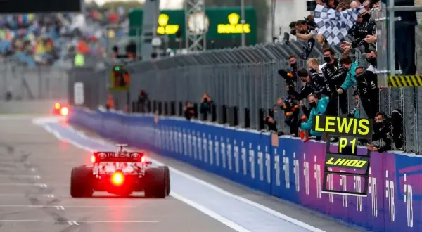 Un coche de Fórmula 1 cruza la meta, con el equipo celebrando la victoria de Lewis Hamilton en el gran premio.