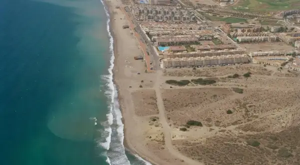 Vista aérea de la playa del Retamar, con el mar turquesa, arena dorada, urbanizaciones y un campo de golf.