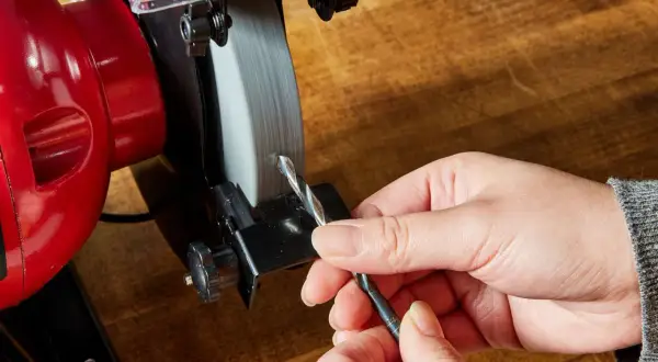 Persona afila brocas en una amoladora.