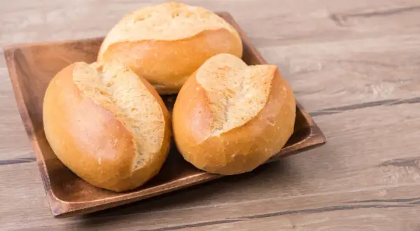 Trzy świeże bułki pszenne na drewnianej desce. Zastanawiasz się nad ich kcal?