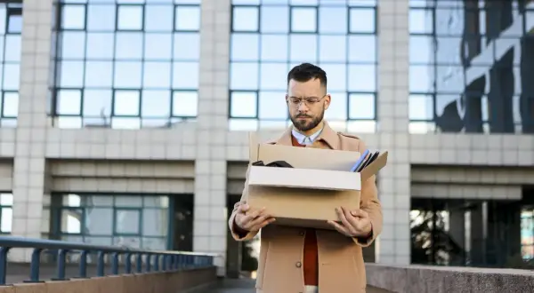 Zmartwiony mężczyzna z kartonem rzeczy po utracie pracy, myślący o spłacie kredytu.