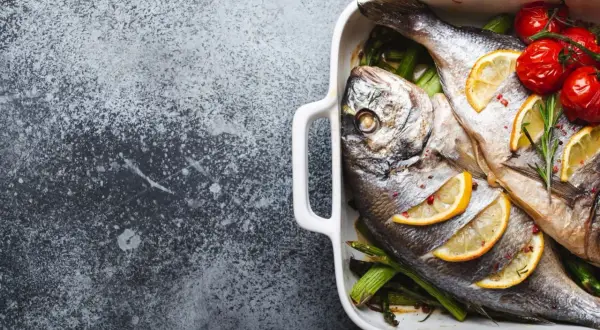 Deux poissons le saint pierre, cuits au four avec des citrons, des tomates cerises et des asperges dans un plat blanc.