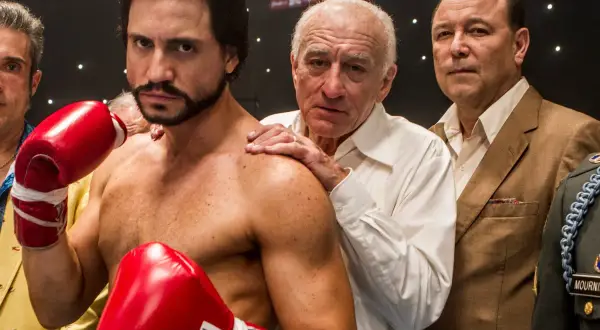 Roberto Duran, the legendary fighter, stands ready with red boxing gloves. His team, including Robert De Niro, offers support.