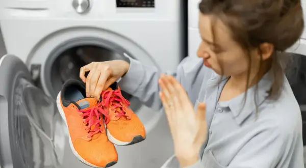 Donna con scarpe arancioni in mano, davanti a una lavatrice aperta. Scopri come lavare le scarpe in lavatrice per farle tornare come nuove.