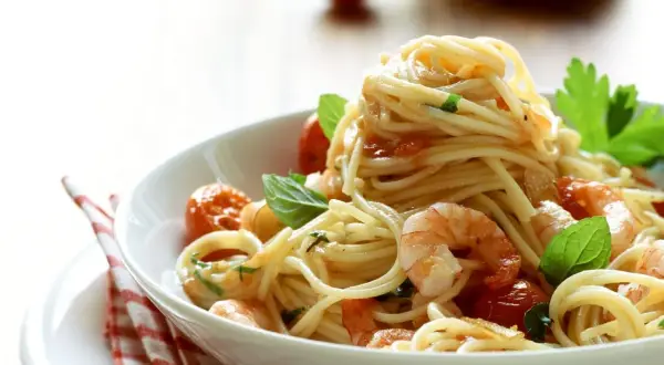 Ein Teller mit köstlichen Spaghetti mit Garnelen, Kirschtomaten und frischem Basilikum, appetitlich angerichtet.