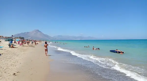 En solig stranddag vid Campofelice di Roccella med folk som badar och kopplar av.