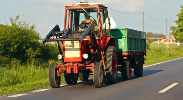 Czerwony traktor z przyczepą jedzie drogą. Zastanawiasz się, ile kosztuje przegląd ciągnika rolniczego?