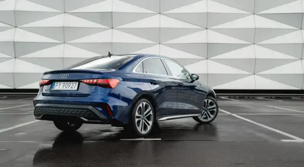 Eleganckie, nowe Audi A3 w kolorze granatowym prezentuje się stylowo na tle nowoczesnej architektury.