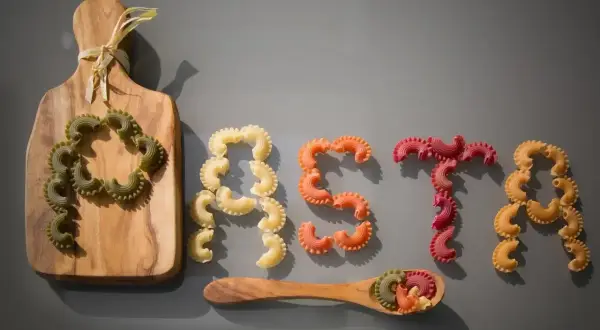 Kolorowy makaron ułożony w napis "PASTA". Kto wymyślił makaron? Może ten, kto ułożył te pyszne kształty na desce i łyżce.