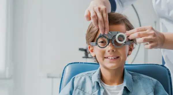 Chłopiec w okularach próbnych podczas badania wzroku u optometrysty.
