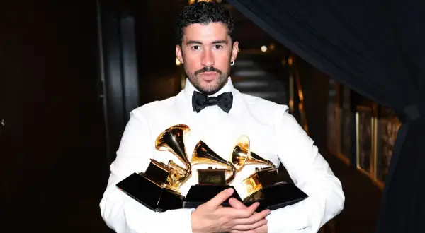 Bad Bunny, ubrany w białą koszulę i czarną muszkę, trzyma kilka złotych nagród Grammy.