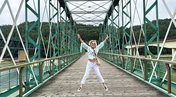 Mujer salta de alegría en un puente verde, disfrutando de las vistas. ¡Un lugar genial que ver en O Vicedo!