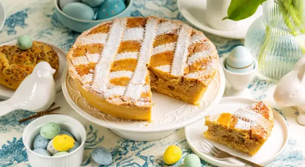Une délicieuse pastiera napoletana saupoudrée de sucre glace, entourée d'œufs de Pâques colorés et d'une décoration printanière.