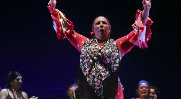 Raquel Heredia, con brazos en alto, luce un traje rojo de lunares blancos y un mantón floral.