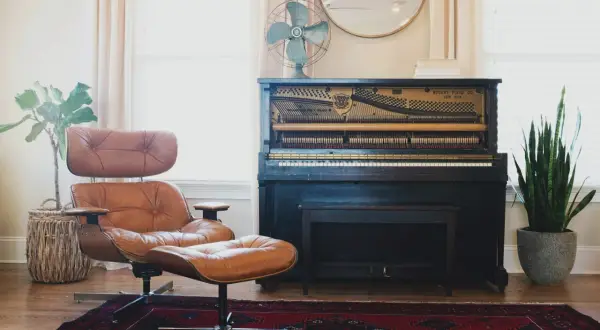 A brown leather armchair and ottoman, a mismatched pair, sit on a Persian rug next to an antique piano.