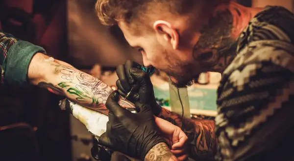 Tatuador con guantes negros trabaja en un brazo, creando un diseño detallado. Las opiniones de la Manuela Tattoo son muy positivas.