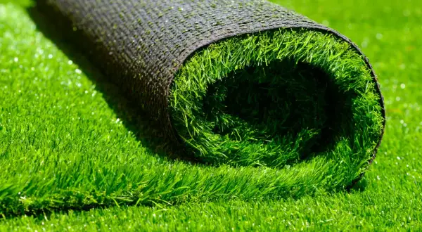 A rolled-up section of artificial grass lies on a bed of lush green turf, hinting at how to install artificial grass for a perfect lawn.