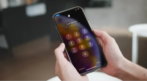 Dłonie trzymające iPhone'a z ekranem blokady i klawiaturą numeryczną.