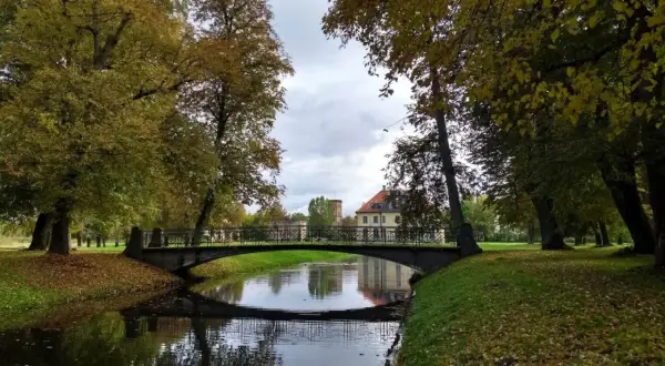 Jesienny park w Choroszczy z mostkiem nad kanałem i pałacem w tle.