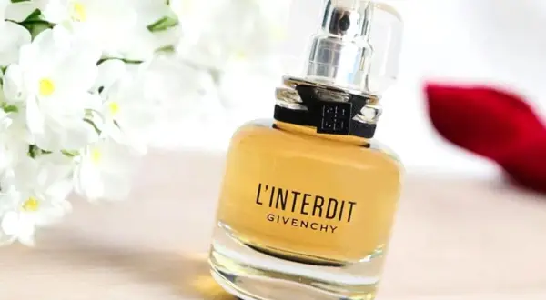 Elegancki flakon perfum L'Interdit Givenchy, otoczony białymi kwiatami i czerwoną szpilką, symbolizuje odwagę i wyrafinowanie.