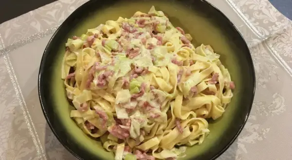 Un plat de tagliatelle poireaux crémeuses avec des lardons, servi dans un bol vert.