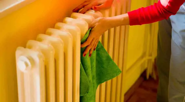 Mani che puliscono un termosifone in ghisa con un panno verde. Il lavaggio interno termosifoni in ghisa è importante per l'efficienza.