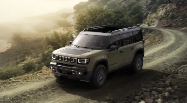 Jeep Recon in verde militare affronta un sentiero sterrato in montagna, pronto per ogni avventura.