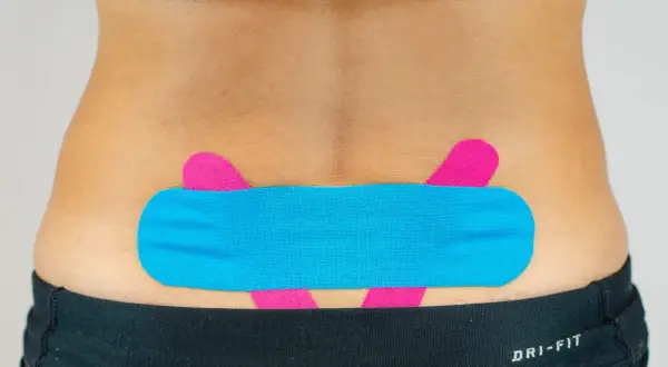 LWS tapen: Blaues und pinkes Kinesio-Tape stützt den unteren Rücken für mehr Stabilität und Schmerzlinderung.